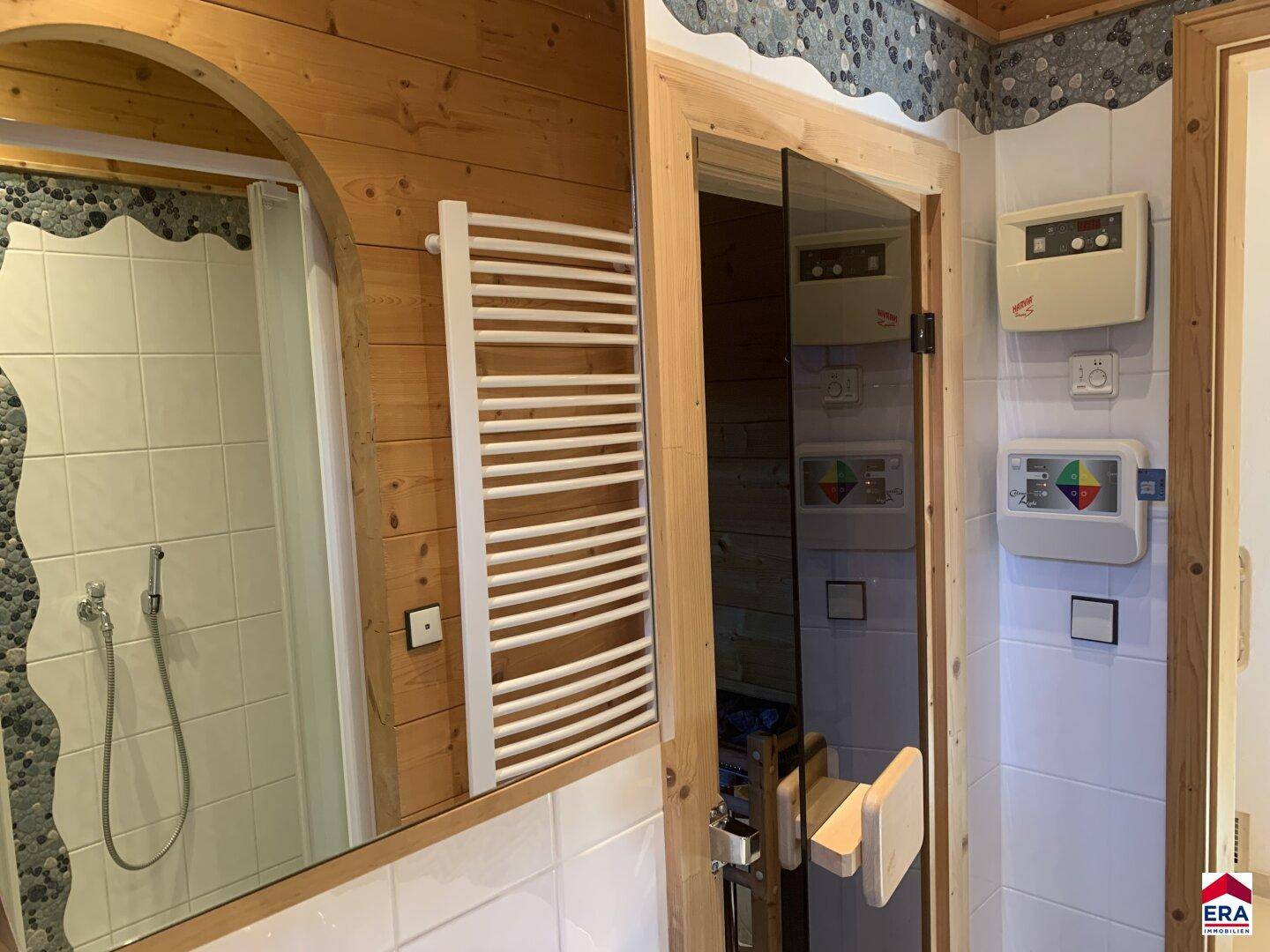 Badezimmer mit Handtuchheizkörper, Spiegel und Zugang zur Sauna.