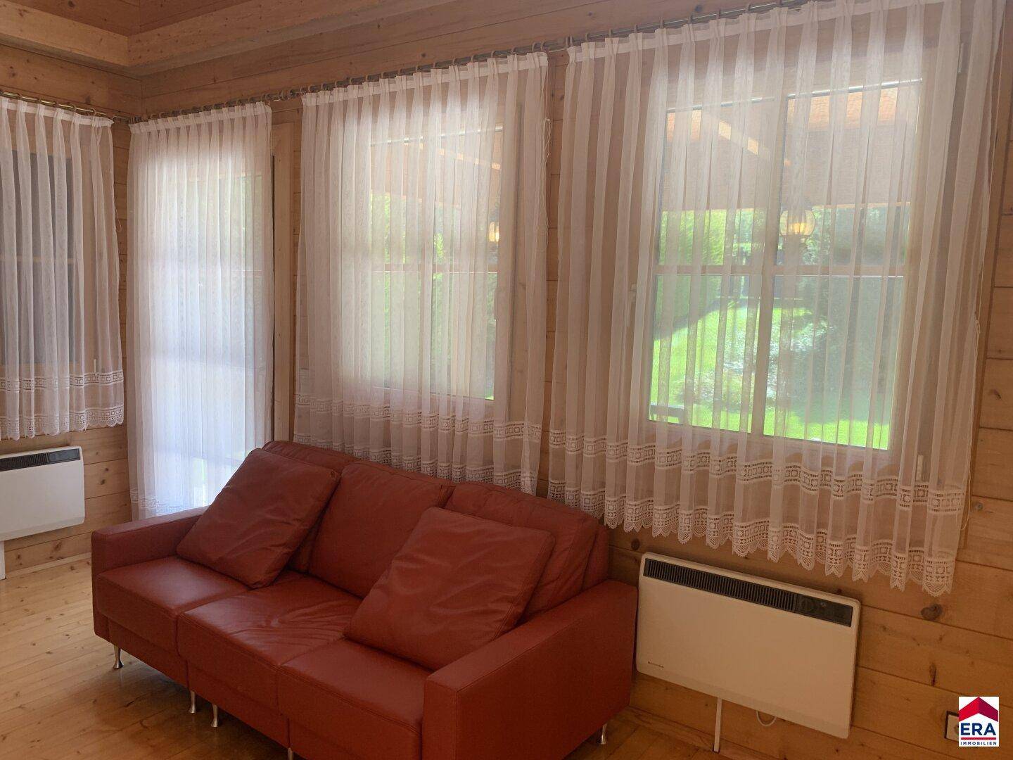 Gemütliches Wohnzimmer mit rotem Sofa, Holzwänden und großen Fenstern.