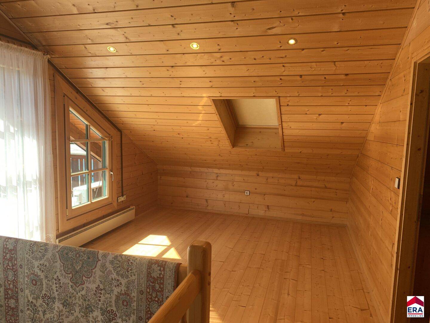Heller Dachbodenbereich mit Holzboden, Dachschräge und Fenster.