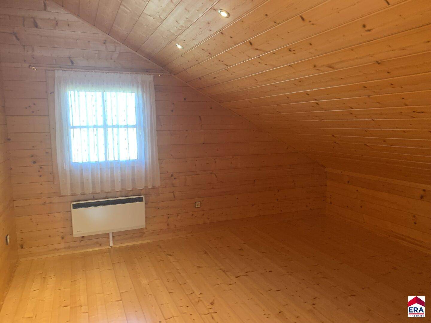 Schlafzimmer im Dachgeschoss mit Holzwänden, Dachschräge und Fenster.
