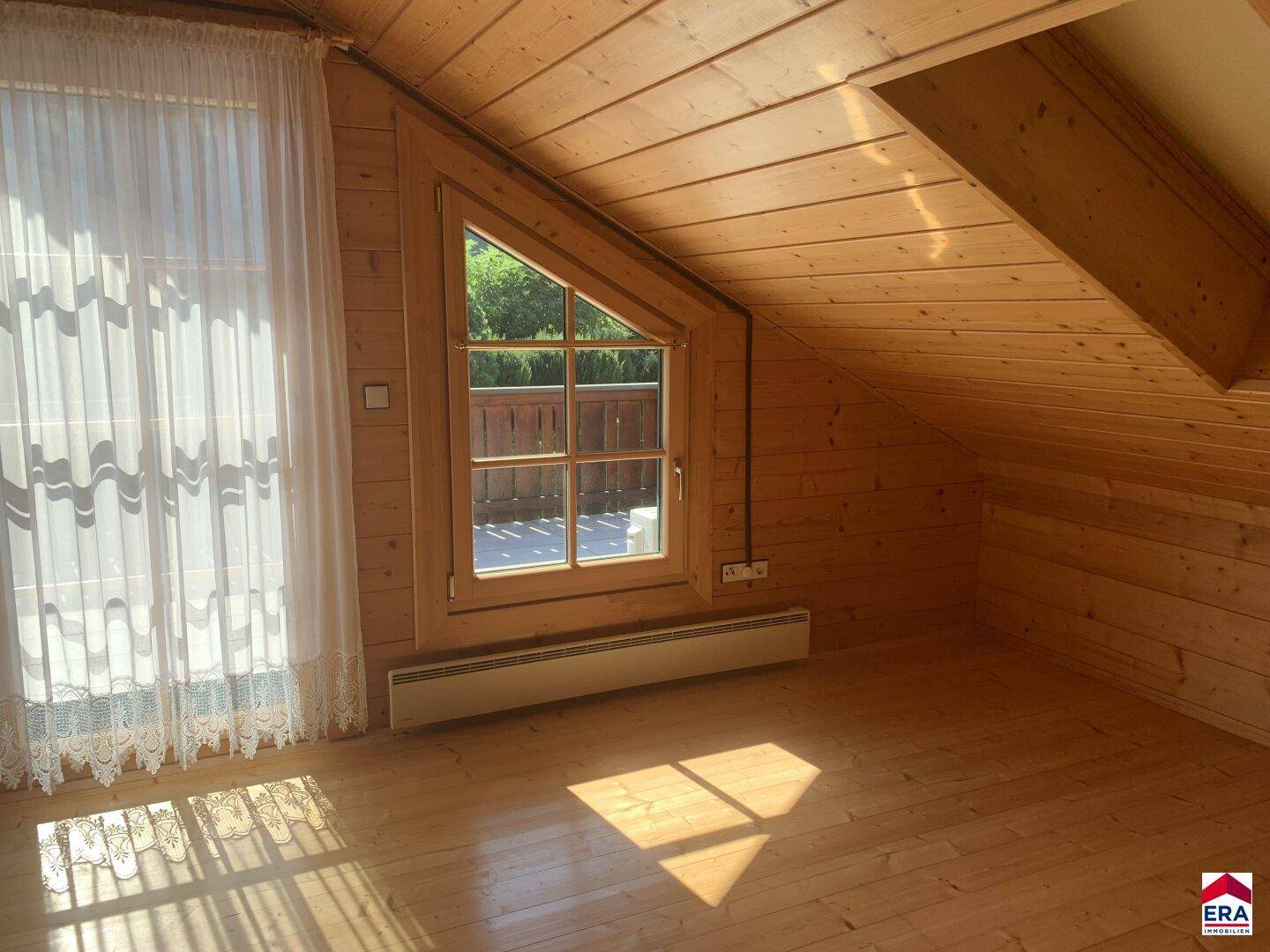 Heller Dachbodenraum mit Holzboden, Dachschräge und Zugang zum Balkon.
