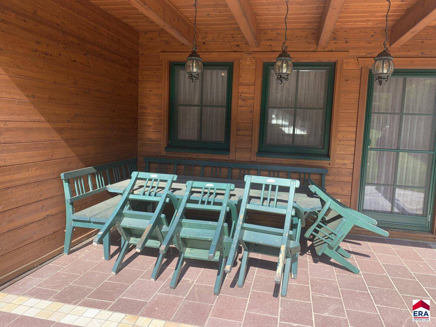 Überdachte Terrasse mit rustikalen Holzmöbeln und Blick auf den Garten.