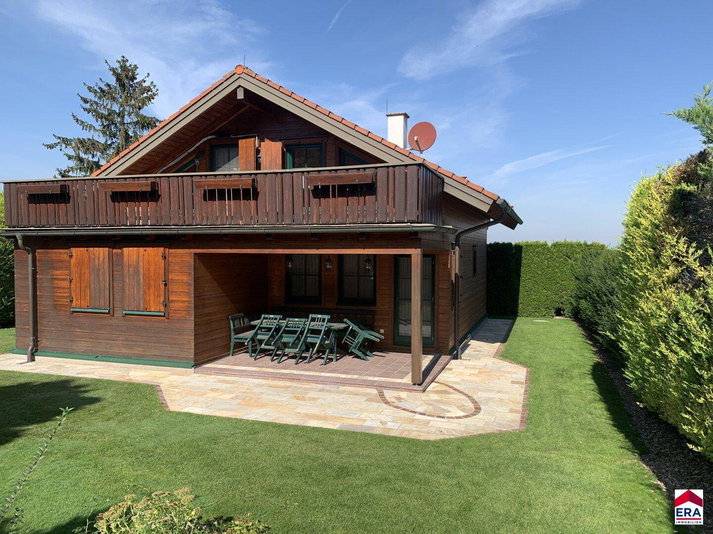 Idyllisches Holzhaus mit großem Garten, Rasenfläche und überdachter Terrasse.