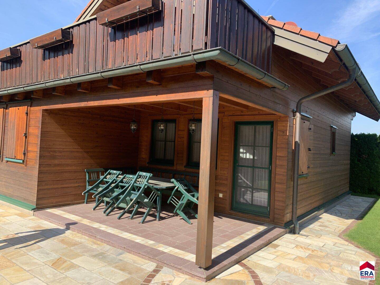 Überdachte Terrasse mit Holzboden und rustikalen Gartenmöbeln am Holzhaus.