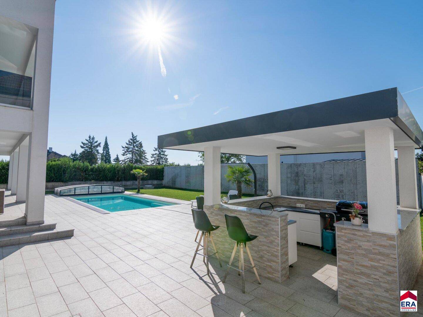 Großzügiger Gartenbereich mit Pool, überdachter Außenküche und Barhockern für entspannte Stunden.