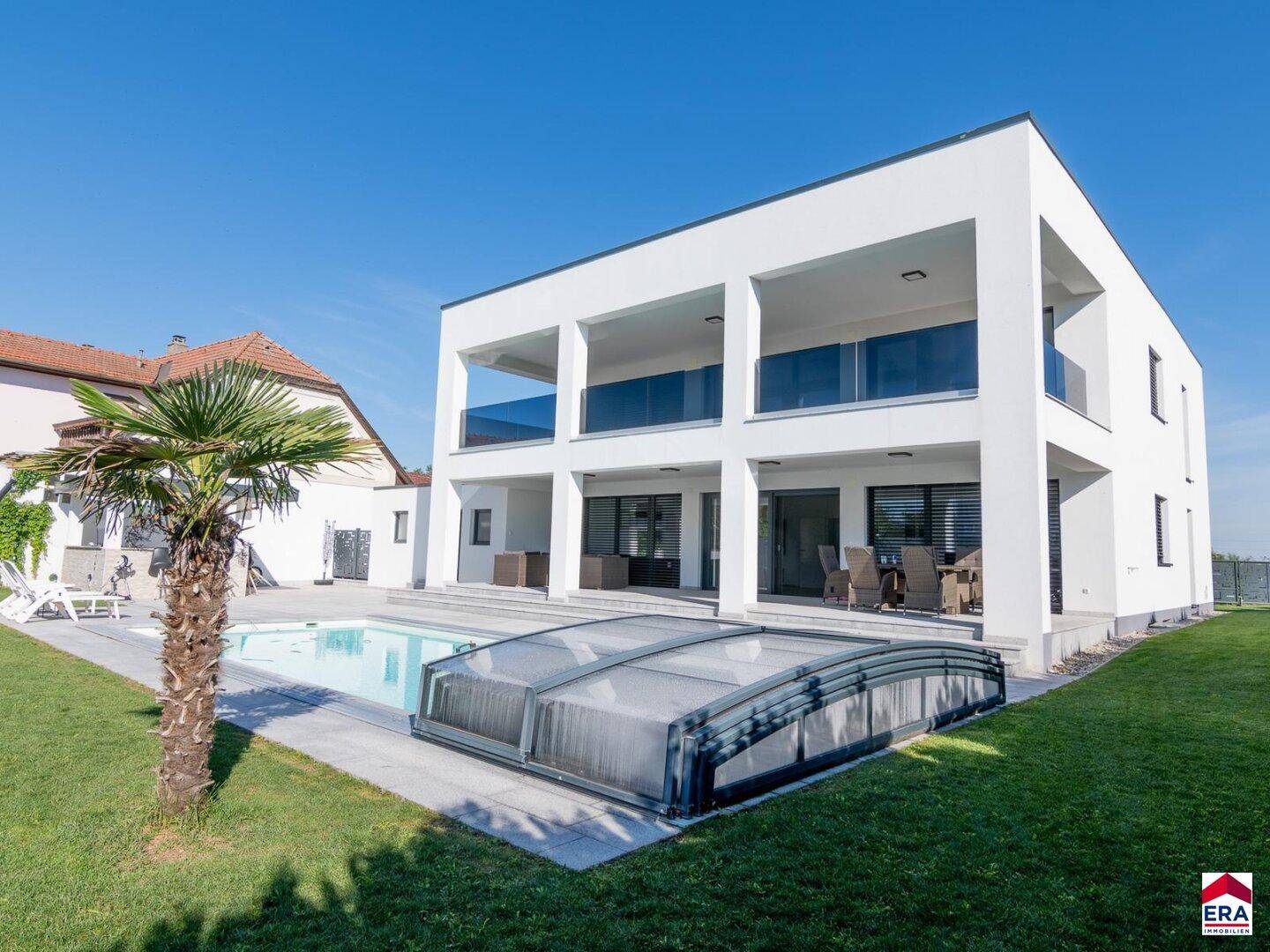 Rückansicht der modernen Villa mit großem Pool, weitläufigem Rasen und mehreren Balkonen.