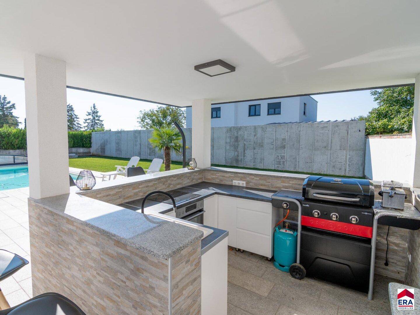 Detailansicht der überdachten Außenküche mit Grill, Spüle und Arbeitsfläche am Poolbereich.