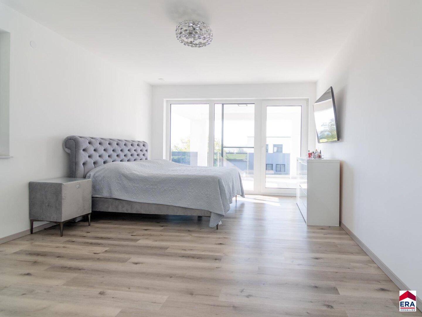 Geräumiges Schlafzimmer mit hellem Boden, großem Bett und Zugang zu einem Balkon oder Terrasse.