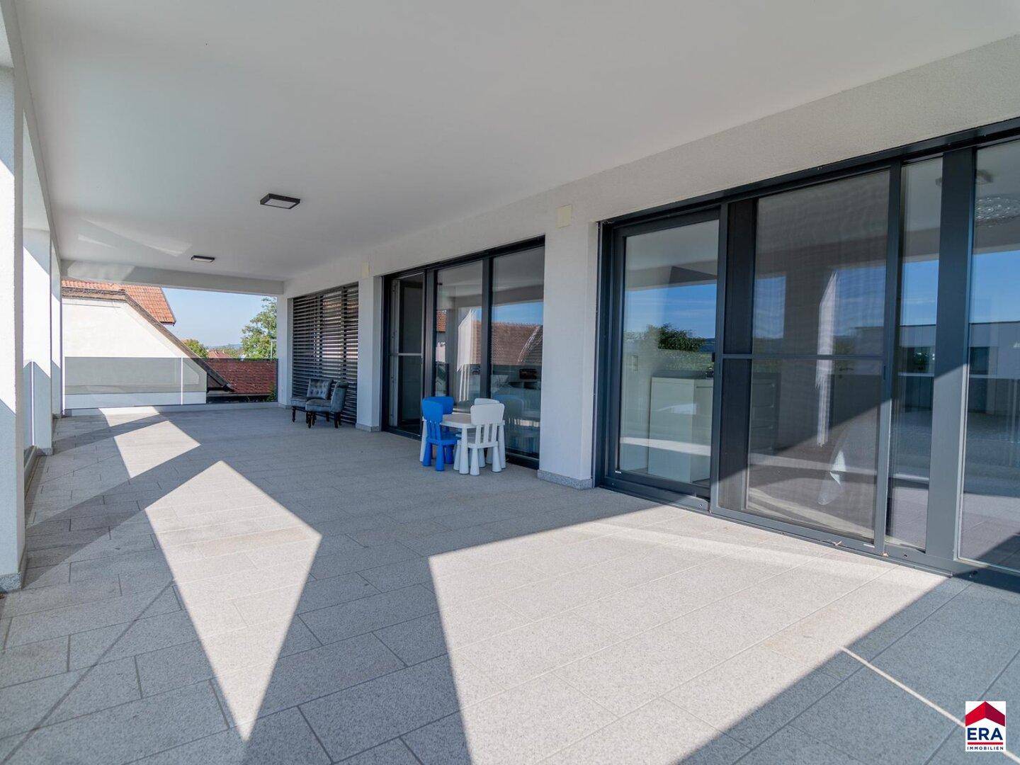 Geräumige überdachte Terrasse mit Fliesenboden und großen Schiebetüren zum Innenbereich.
