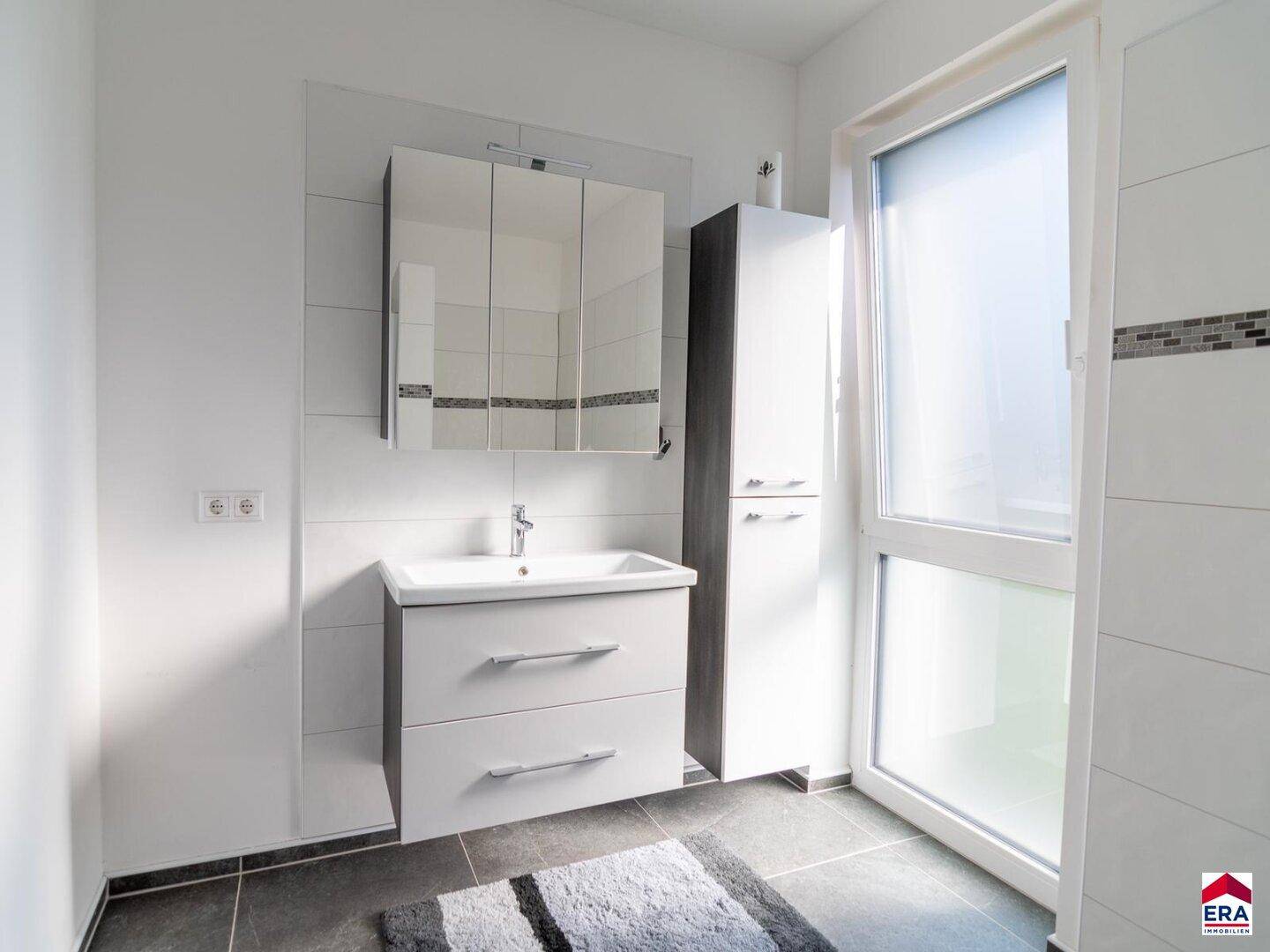 Modernes Badezimmer mit Waschtisch, Spiegelschrank und Fenster für Tageslicht.