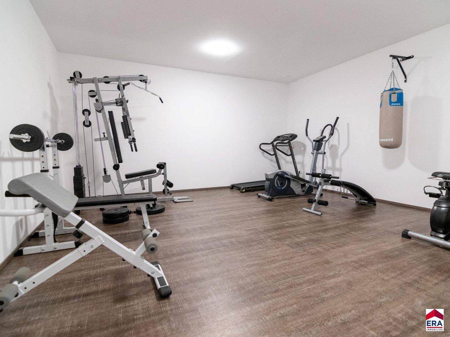Gut ausgestatteter Fitnessraum mit verschiedenen Trainingsgeräten und Boxsack.
