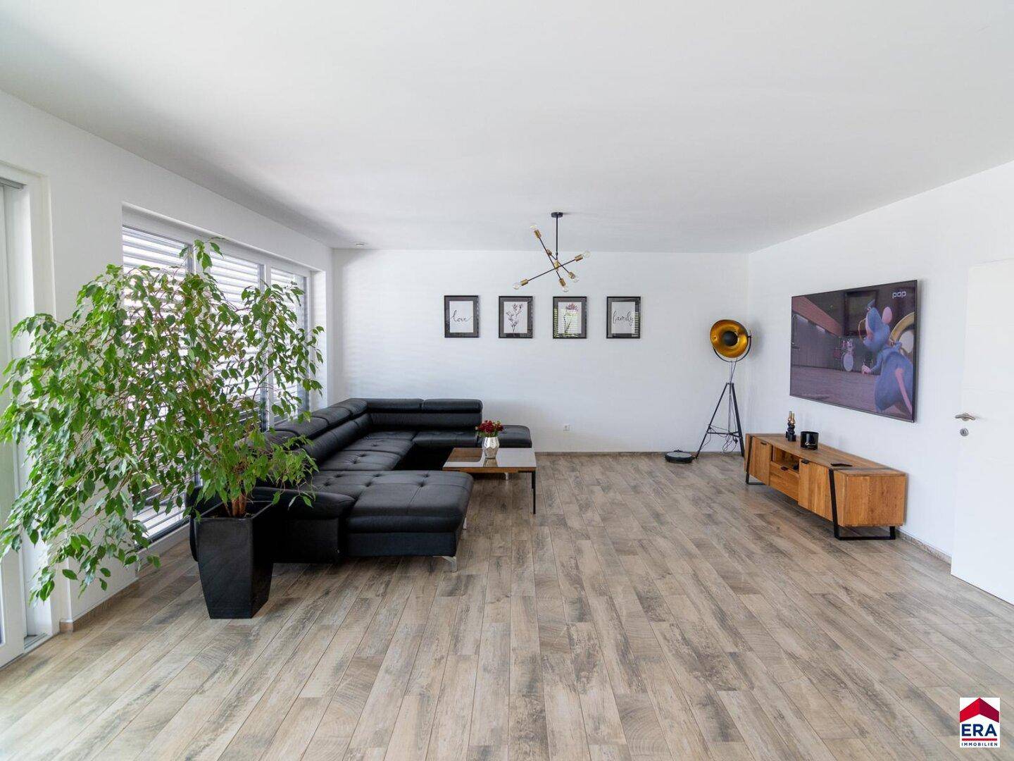 Helles Wohnzimmer mit großem Ecksofa, Holzoptik-Boden und Zugang zu großen Fenstern.
