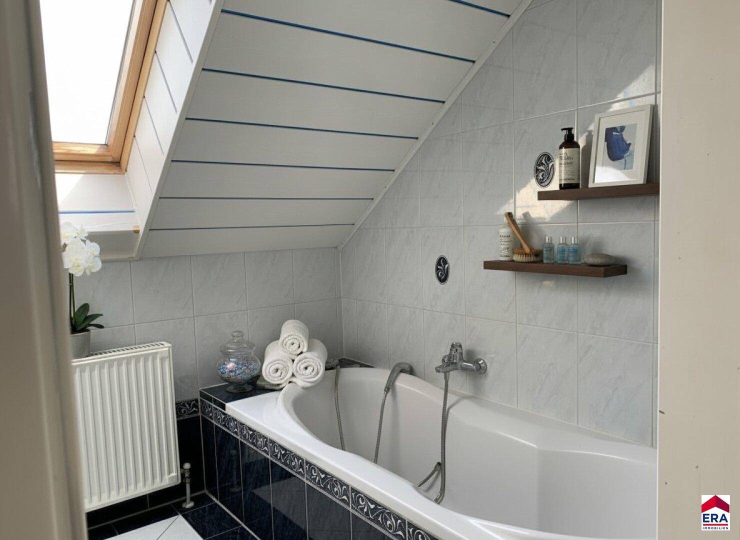 Badezimmer im Dachgeschoss mit Badewanne, Dachfenster und weiß-blauen Fliesen.