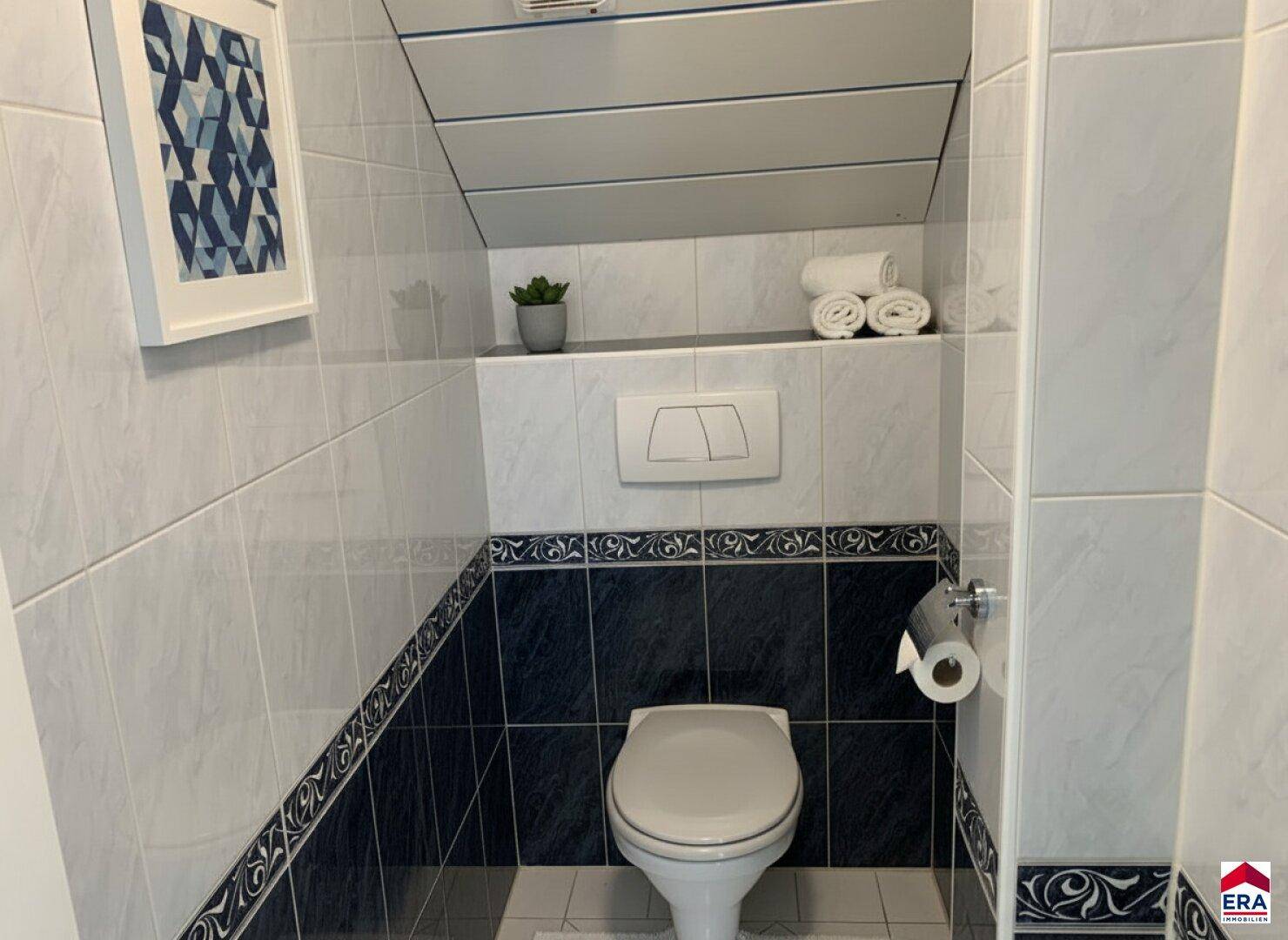 Separate Toilette mit Wand-WC und weiß-blauen Fliesen im Dachgeschoss.