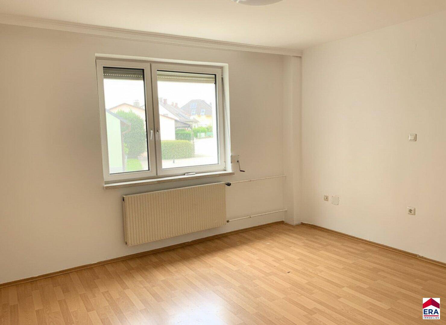 Leeres Zimmer mit Laminatboden, weiß gestrichenen Wänden und einem Fenster mit Rollladen.