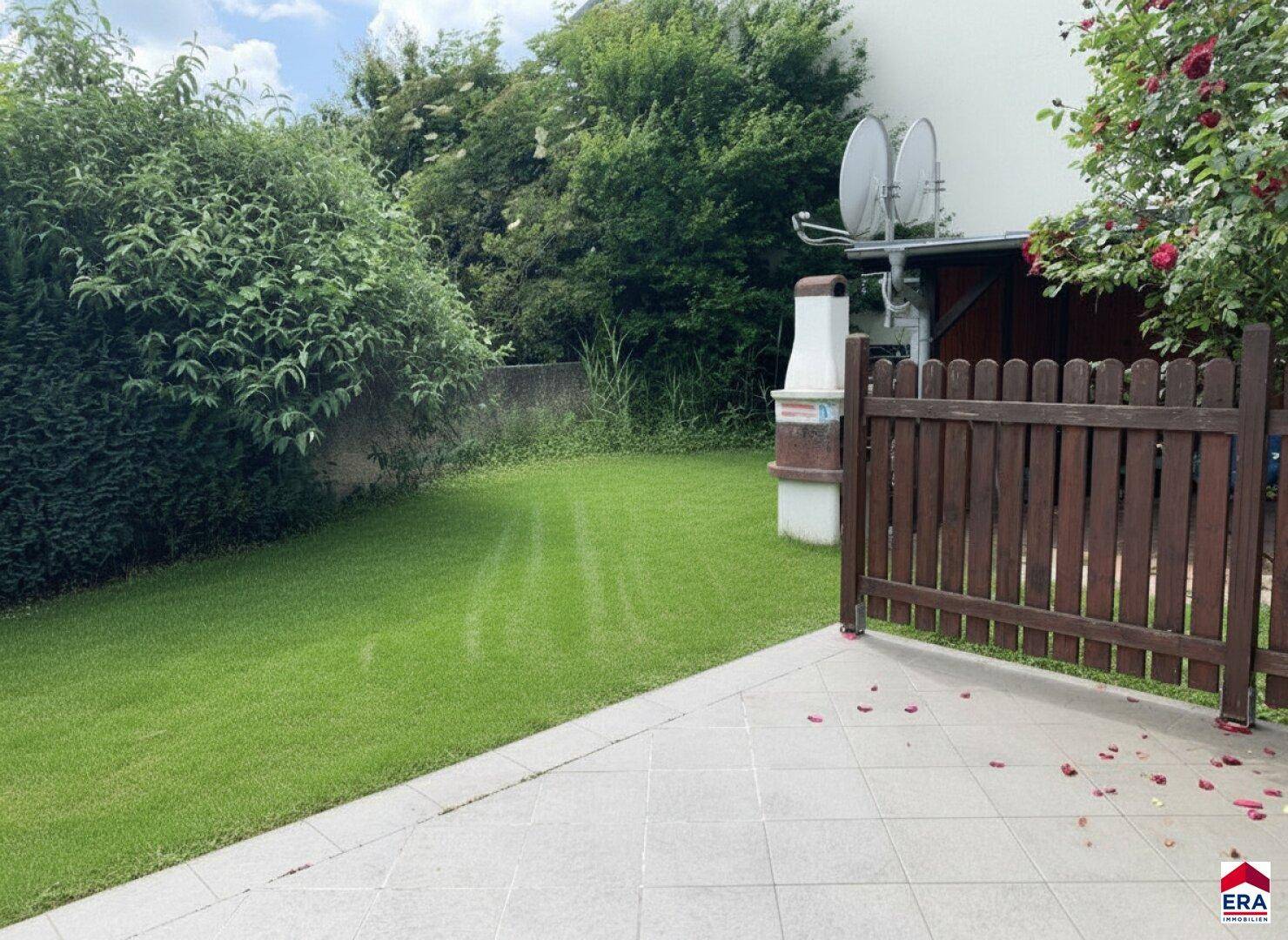 Gepflegter Gartenbereich mit Rasenfläche, Sträuchern und einem gemauerten Grillplatz.