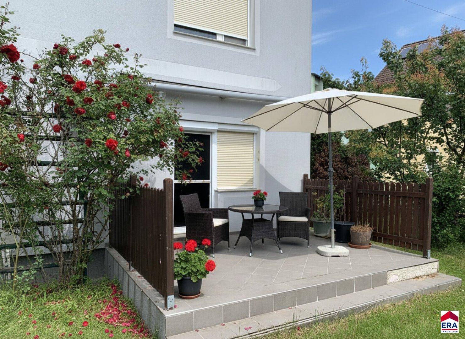 Gemütliche Terrasse mit Gartenmöbeln, Sonnenschirm und blühenden Rosenbüschen im Garten.