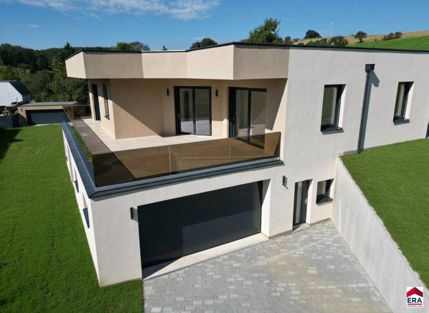 Moderne Hausfassade mit offener Garage, großer Terrasse und gepflegtem Rasen in sonniger Lage.