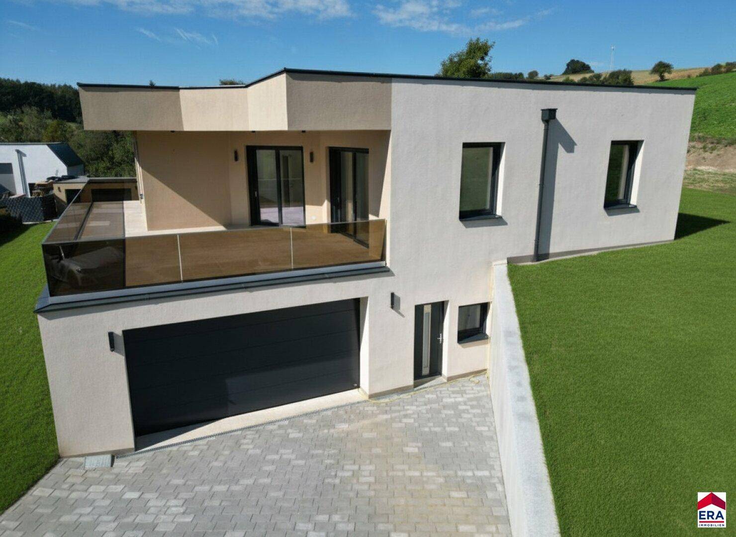 Seitenansicht des modernen Neubaus mit großen Fenstern, Terrasse und Blick auf die grüne Landschaft.
