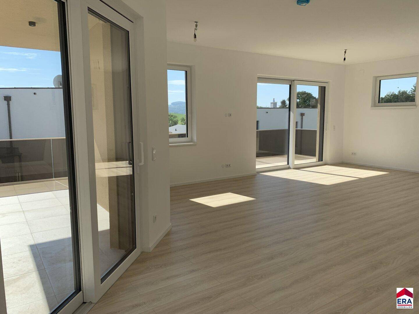 Heller, offener Wohnbereich mit Laminatboden, großen Fenstern und direktem Zugang zur Terrasse.