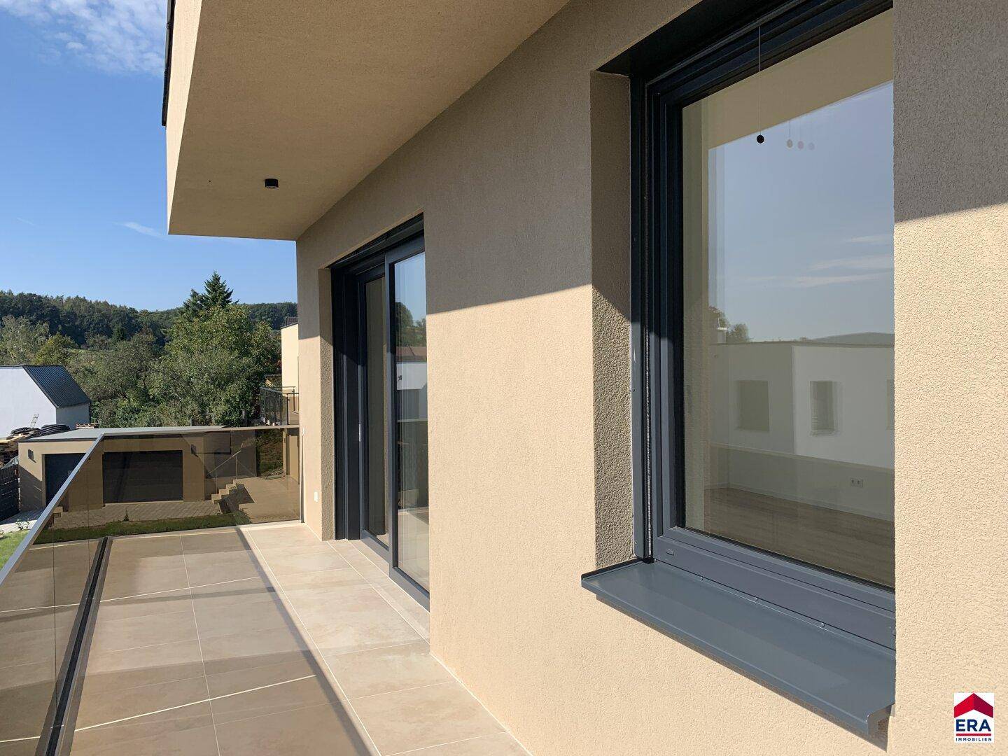 Detailansicht der Terrasse mit Fliesenboden und großen Schiebetüren, die den Innenraum verbinden.