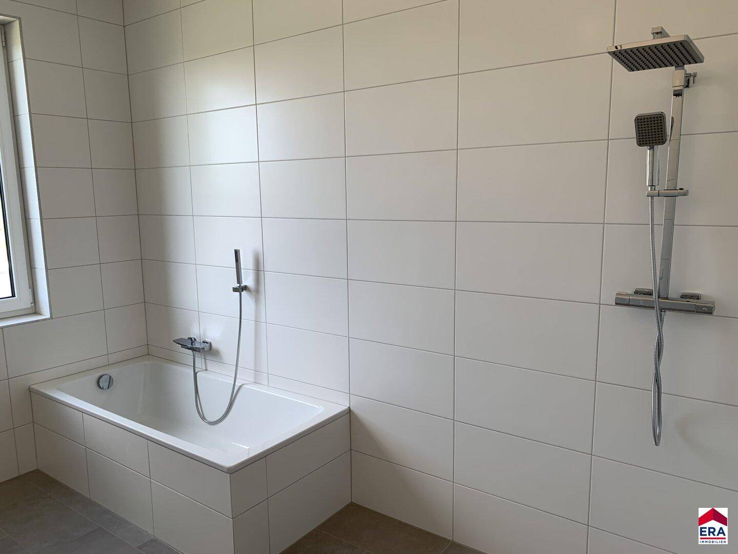 Modernes Badezimmer mit Badewanne, Regendusche, weißen Fliesen und einem Fenster für Tageslicht.