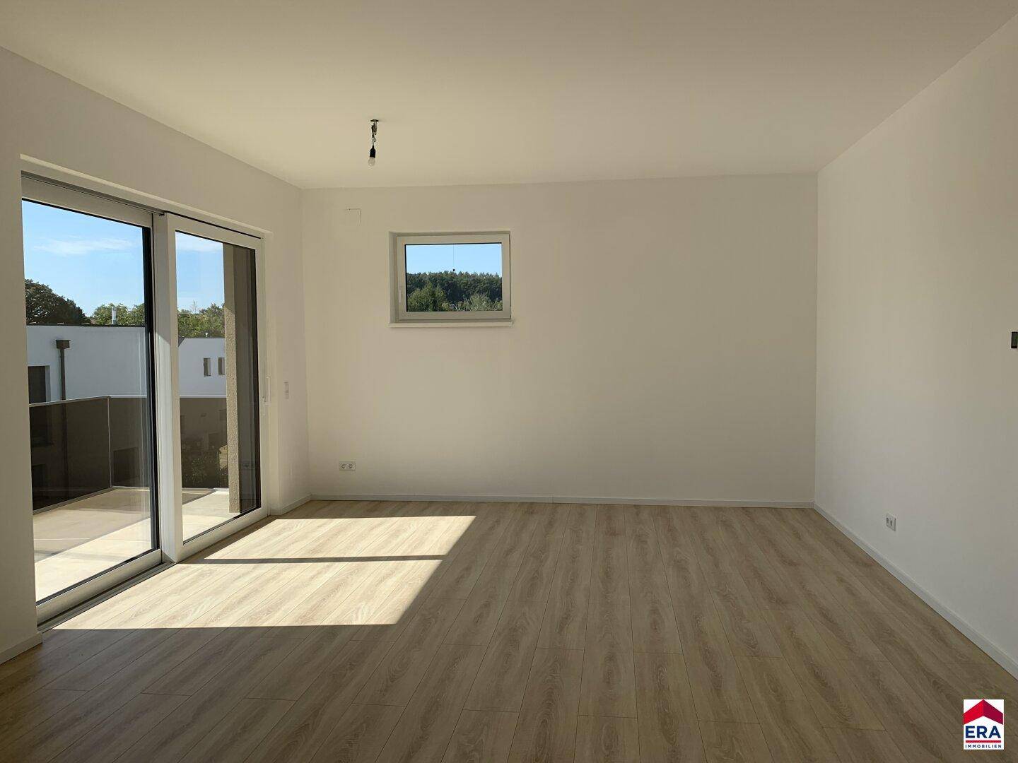 Helles, leeres Wohnzimmer mit Laminatboden, großen Schiebetüren und Zugang zur Terrasse.