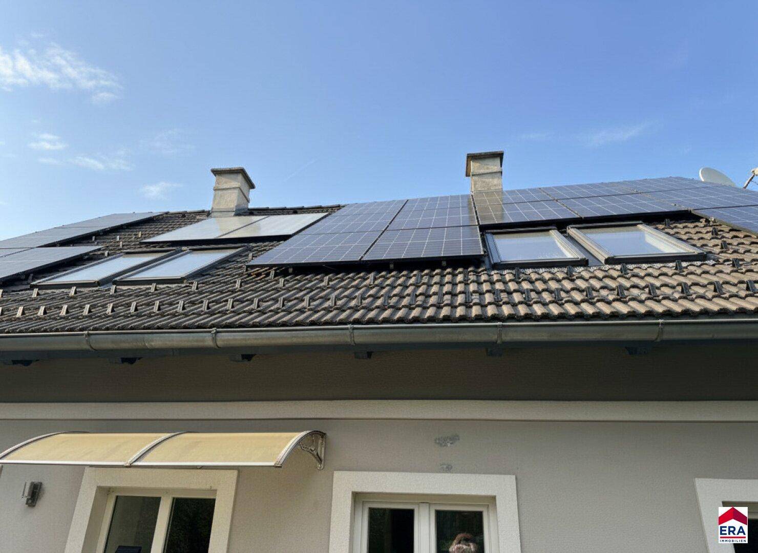 Dachansicht eines Hauses mit Photovoltaikanlage und Dachfenstern unter blauem Himmel.