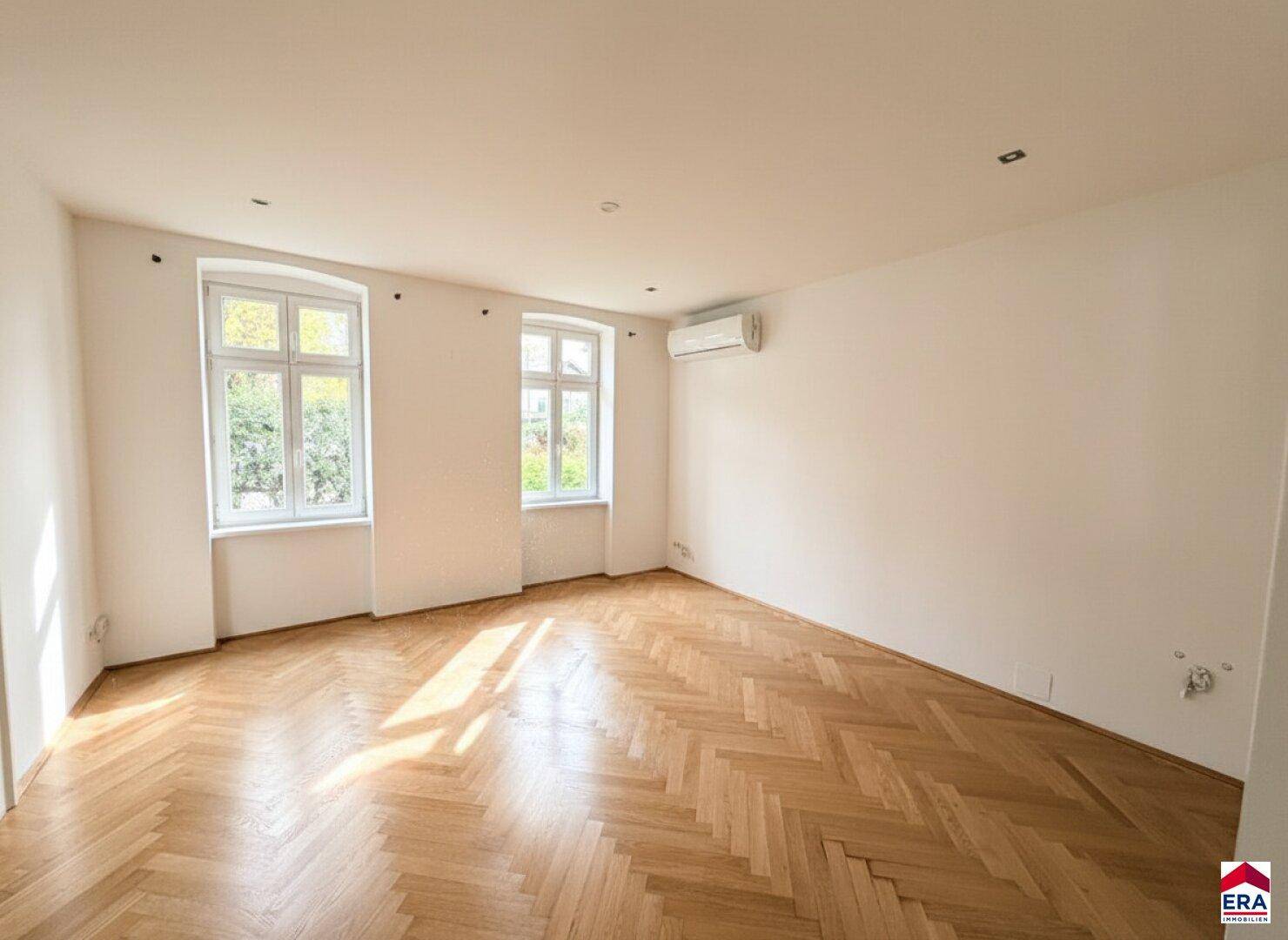 Geräumiger, heller Raum mit Fischgrätparkett, großen Fenstern und Klimaanlage.