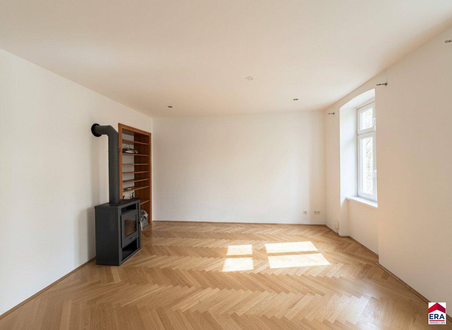 Heller Raum mit Fischgrätparkett und modernem Holzofen, ideal für gemütliche Abende.