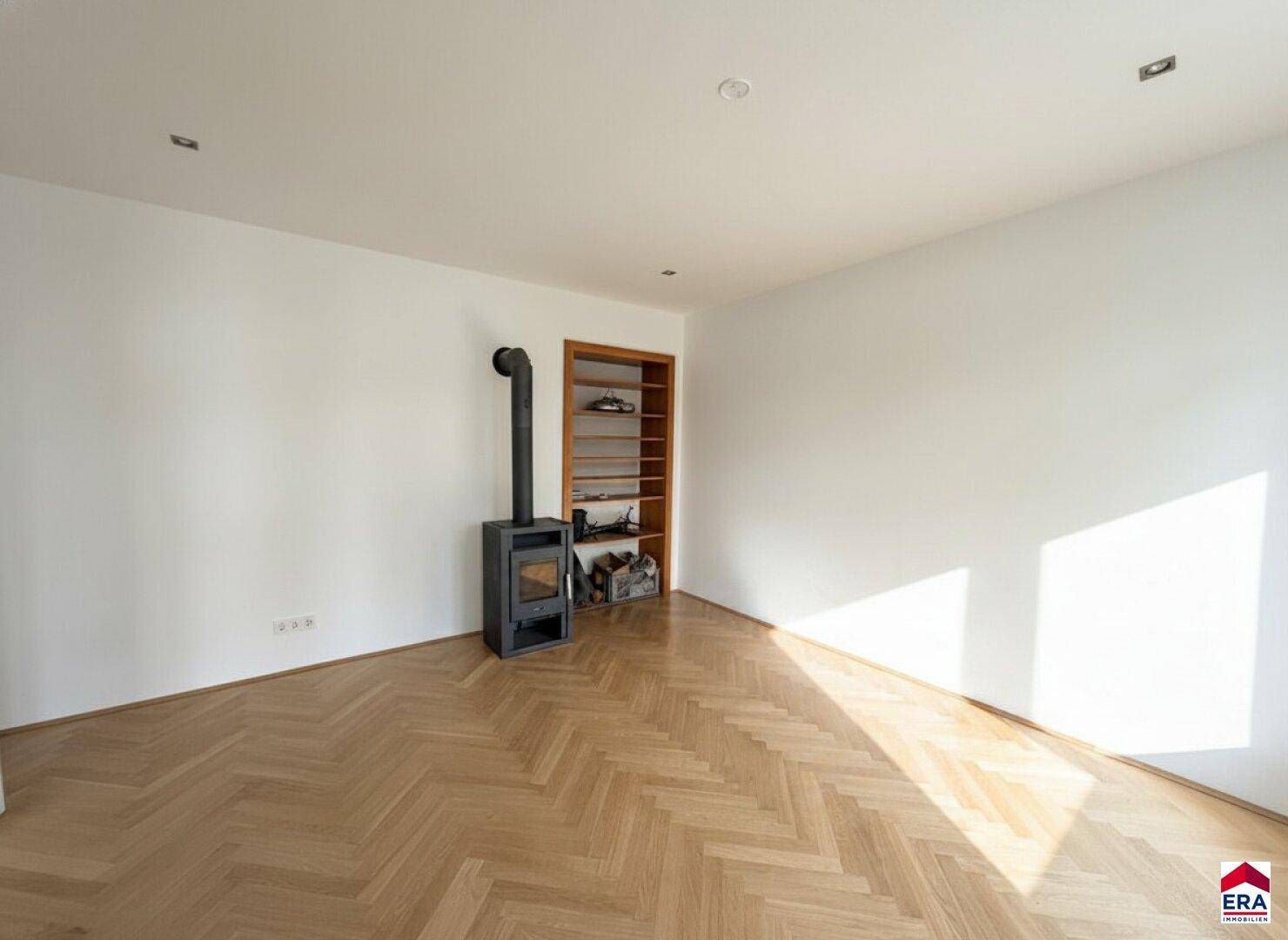 Lichtdurchfluteter Raum mit Fischgrätparkett und elegantem Holzofen, bereit zur Einrichtung.