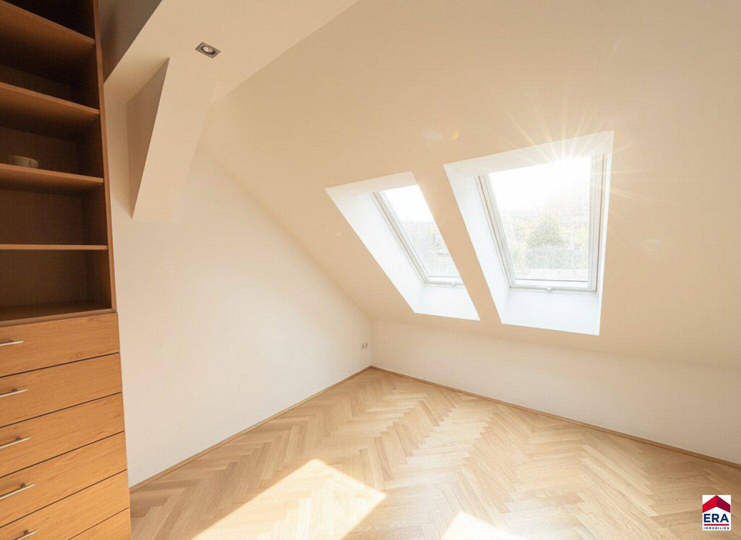 Helles Dachzimmer mit Fischgrätparkett, Einbauregalen und viel natürlichem Licht.