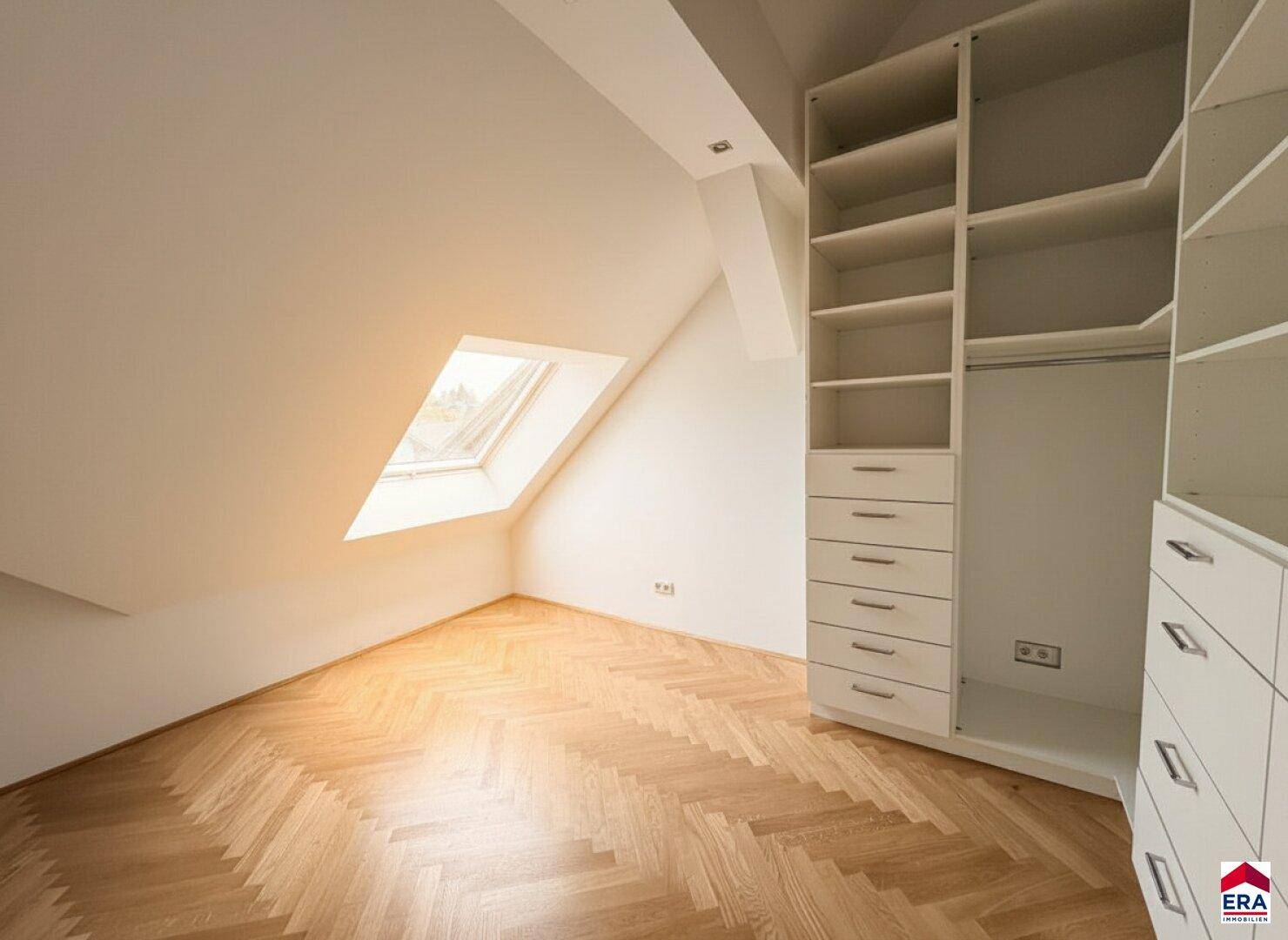 Dachgeschossraum mit Fischgrätparkett und praktischen Einbauschränken unter dem Dachfenster.