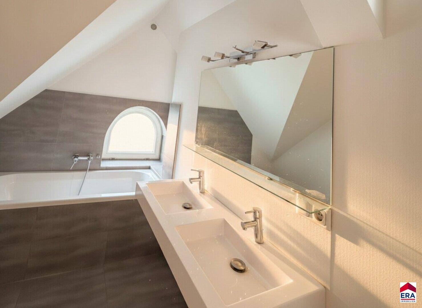 Helles Dachgeschossbad mit Doppelwaschbecken, großem Spiegel und Badewanne.