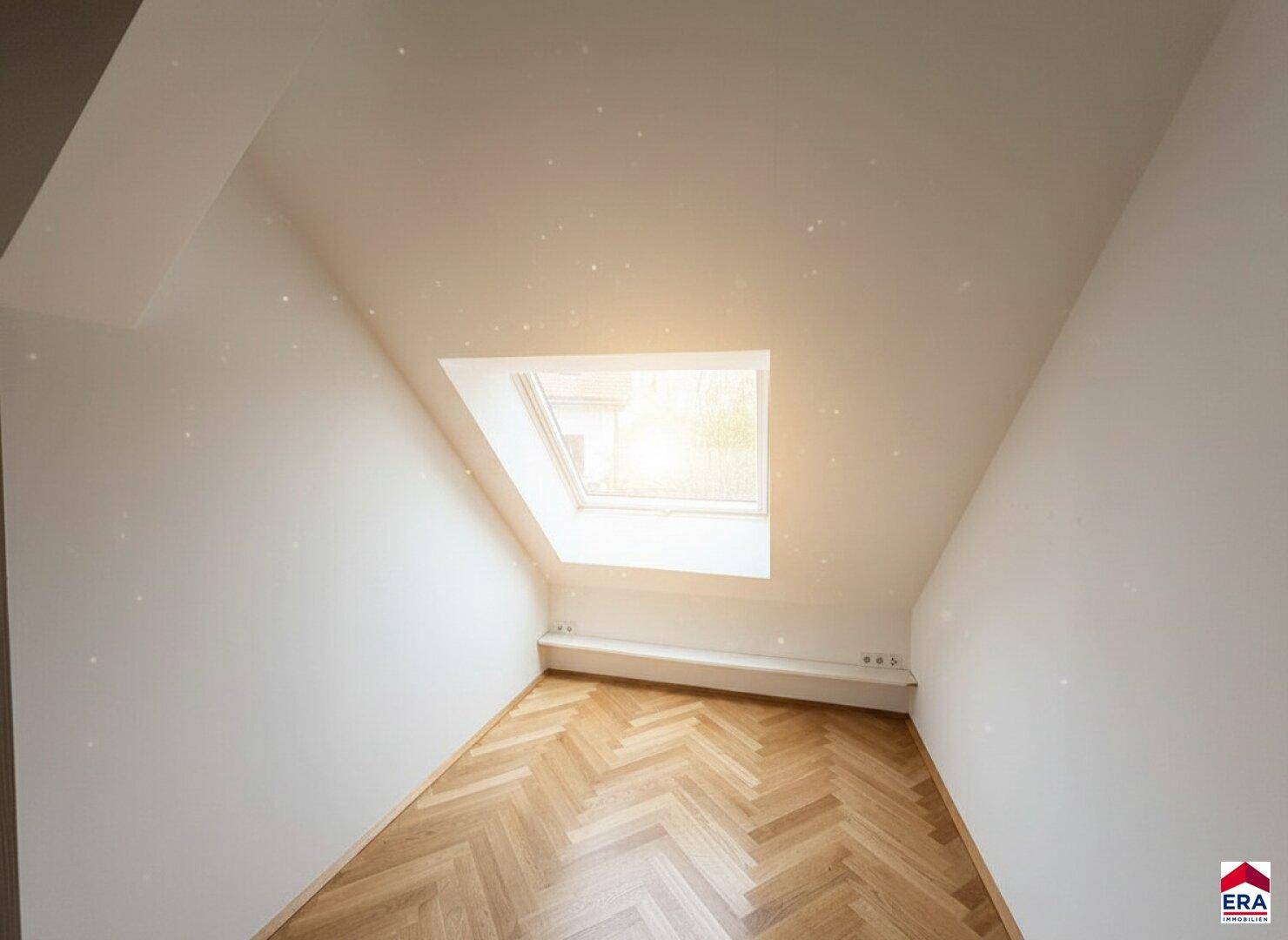 Kleiner, heller Dachgeschossraum mit Fischgrätparkett und einem Dachfenster.