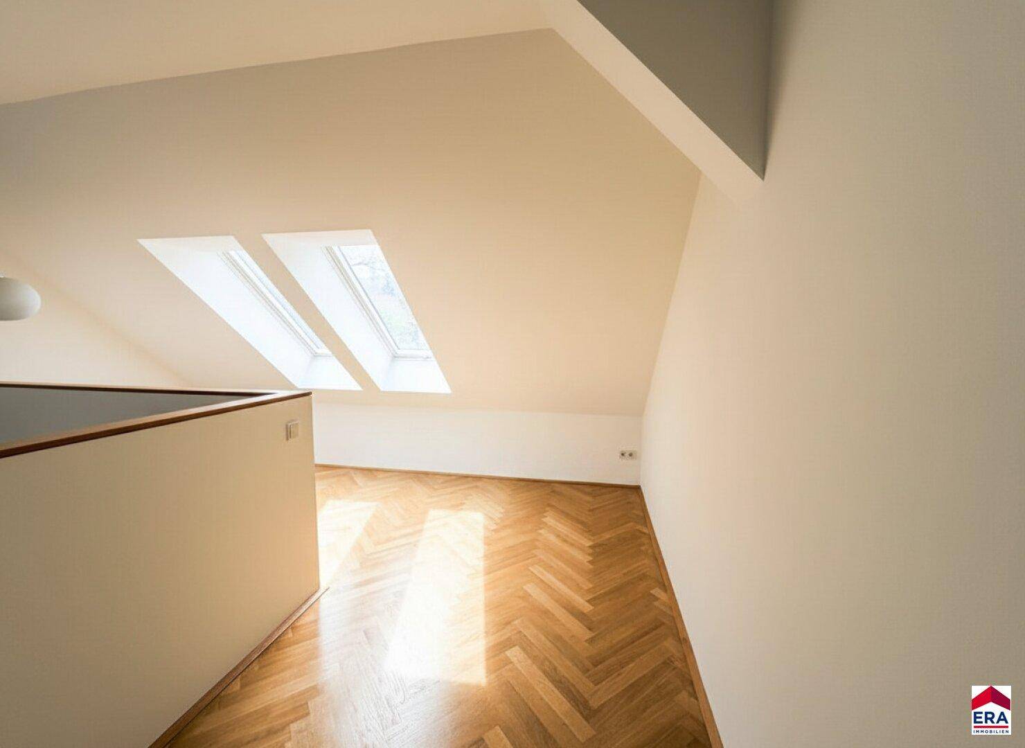 Geräumiges Dachzimmer mit Fischgrätparkett und zwei großen Dachfenstern.