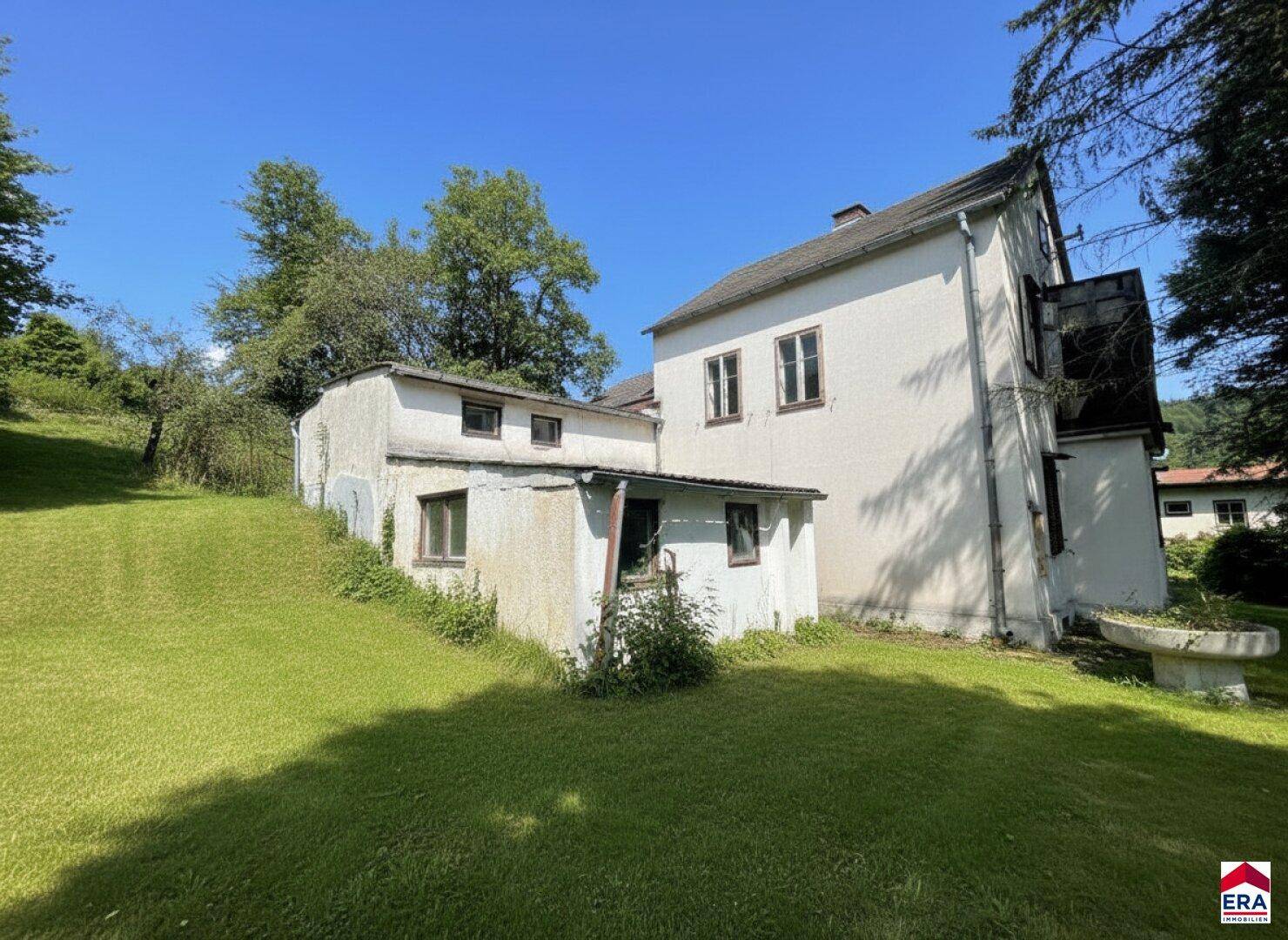 Seitenansicht eines älteren Gebäudes mit Anbau und grüner Rasenfläche im Vordergrund.