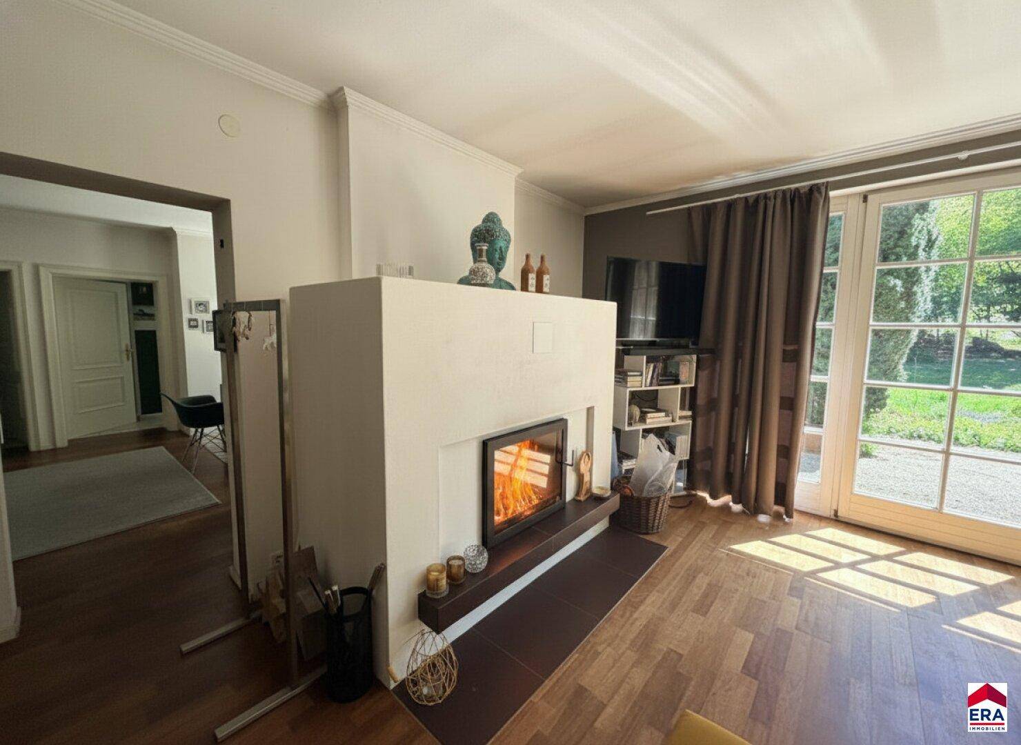 Gemütliches Wohnzimmer mit Kamin, Holzboden und großen Fenstern zum Garten.
