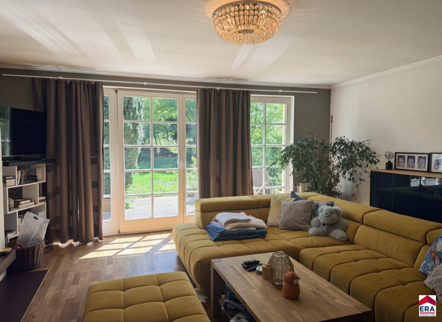 Helles Wohnzimmer mit bequemer gelber Couch und weitem Blick in den grünen Garten.