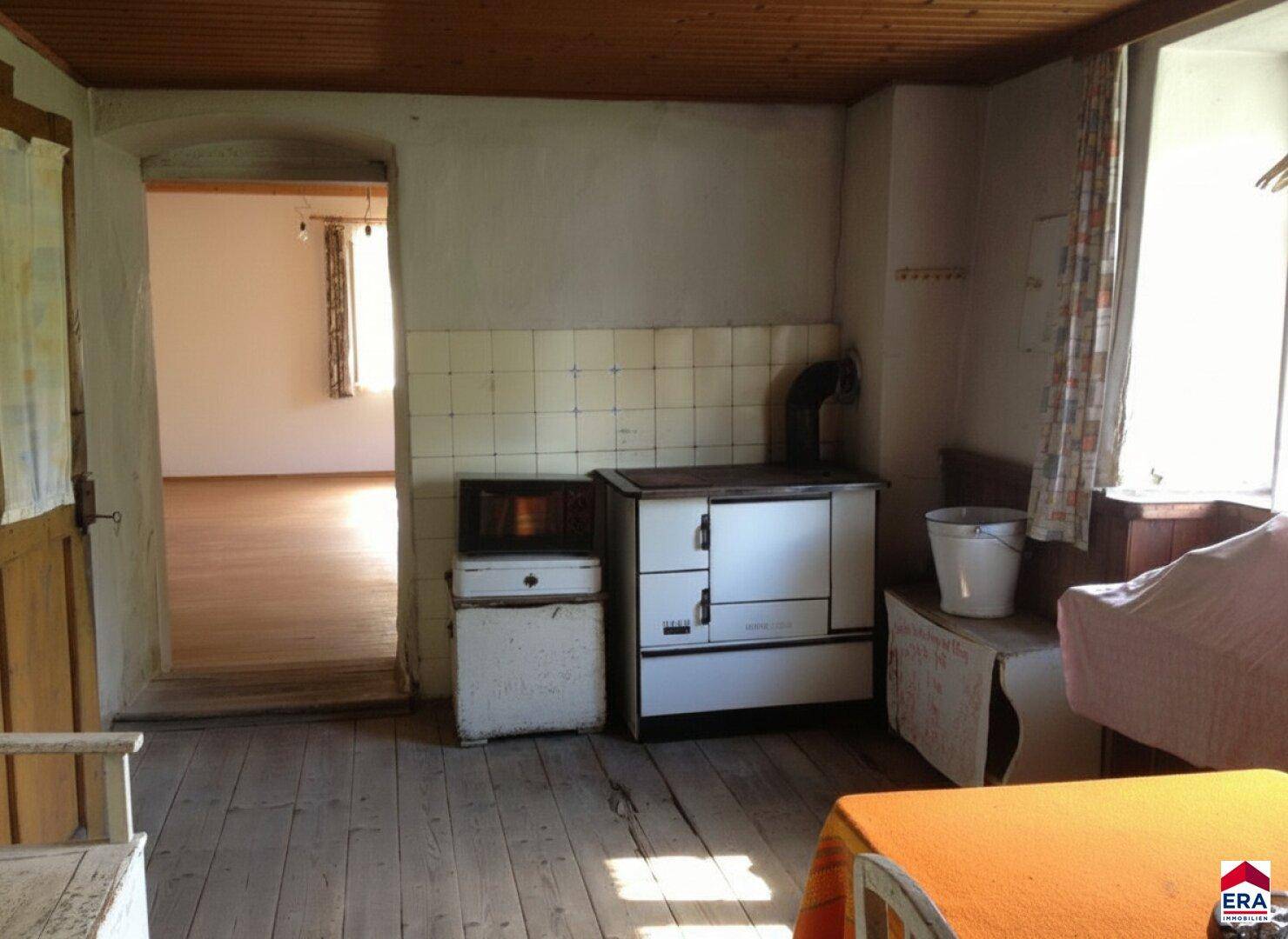 Traditionelle Küche mit einem alten Holzofen und gefliestem Bereich, bereit für eine Modernisierung.