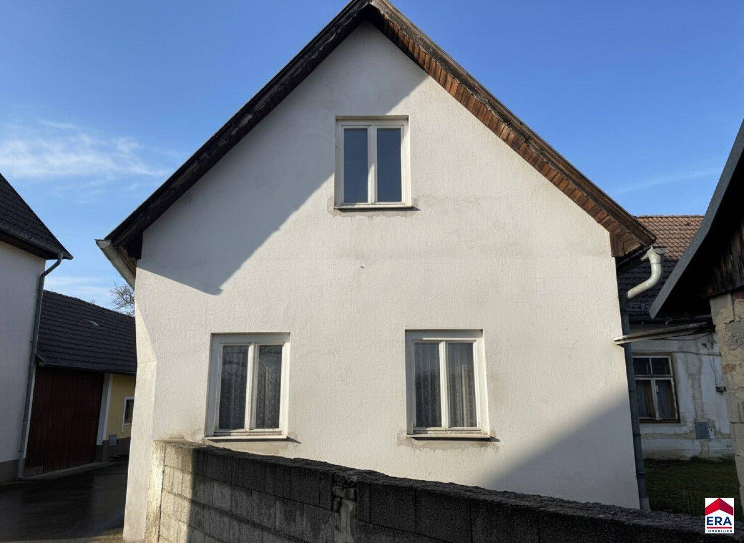 Vorderansicht des Hauses mit weißer Fassade, drei Fenstern und einem traditionellen Ziegeldach.