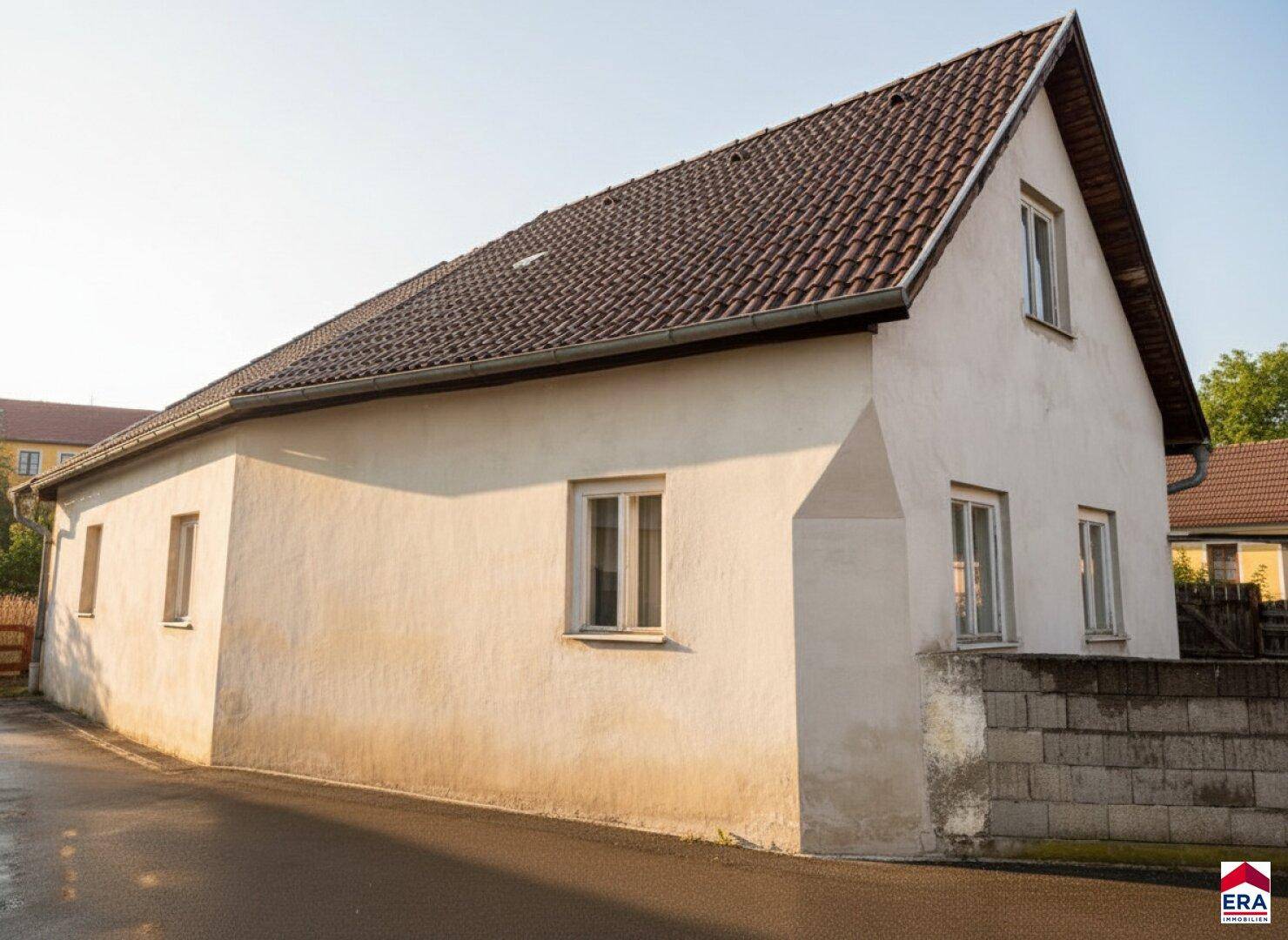 Seitenansicht des Hauses mit weißer Putzfassade und klassischem Satteldach unter blauem Himmel.