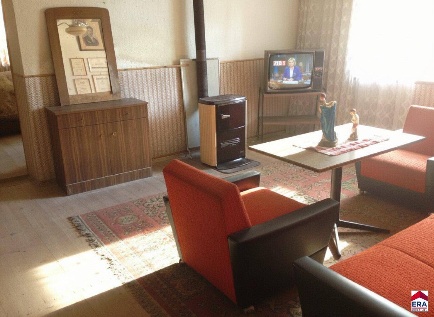 Gemütliches Wohnzimmer mit Vintage-Möbeln, einem kleinen Holzofen und Holzdielenboden.