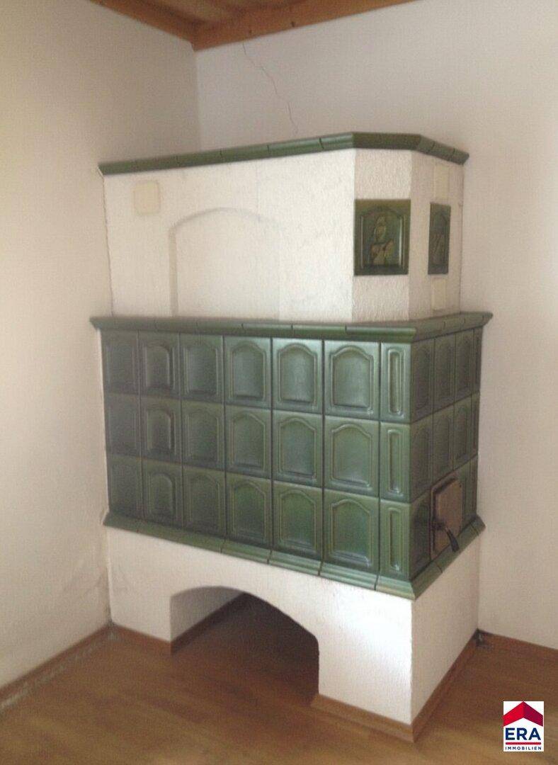 Traditioneller grüner Kachelofen in einer Ecke des Raumes, der Wärme und Gemütlichkeit spendet.