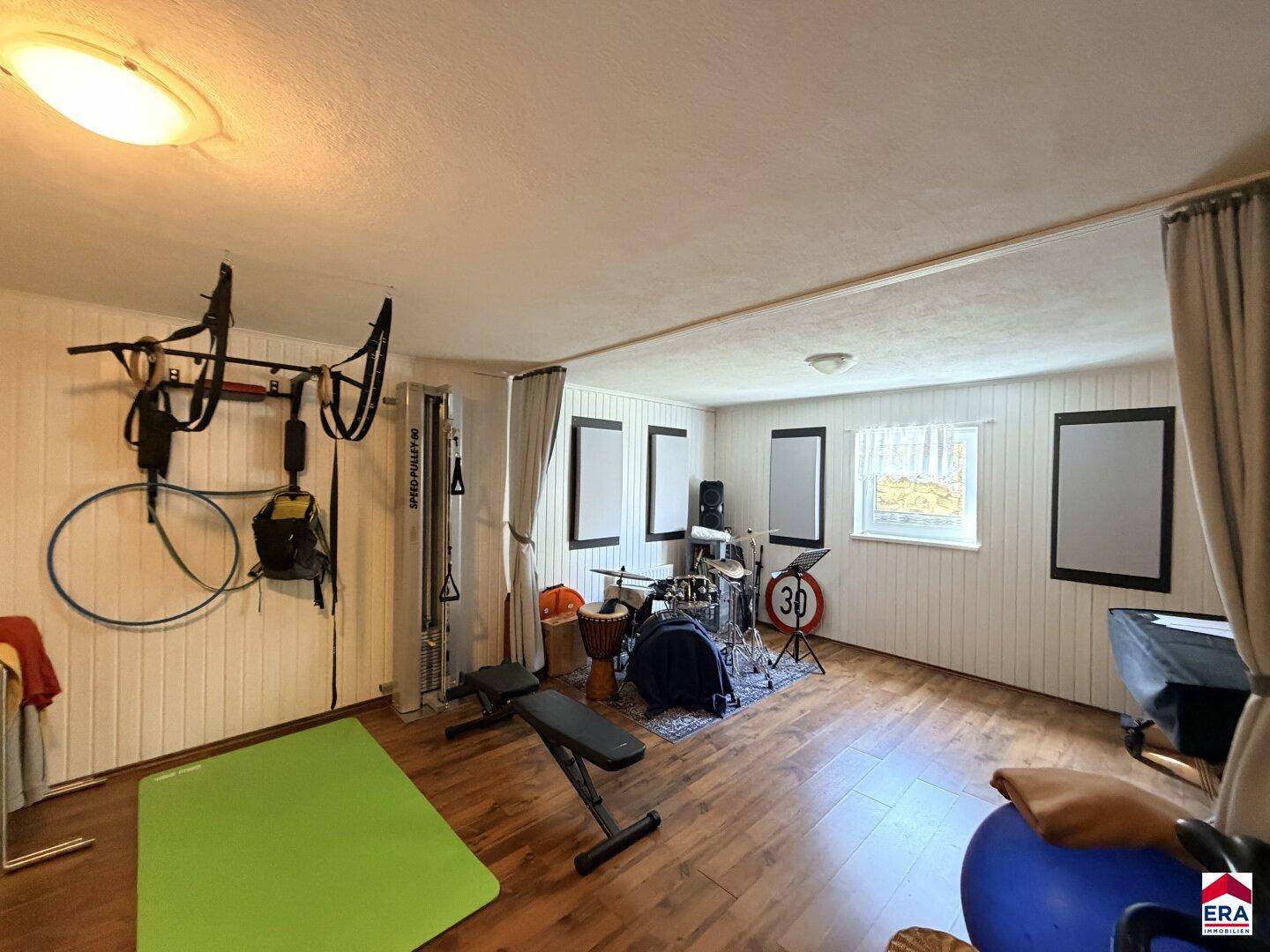 Vielseitiger Hobbyraum mit Fitnessgeräten, Musikinstrumenten und Holzoptikboden.