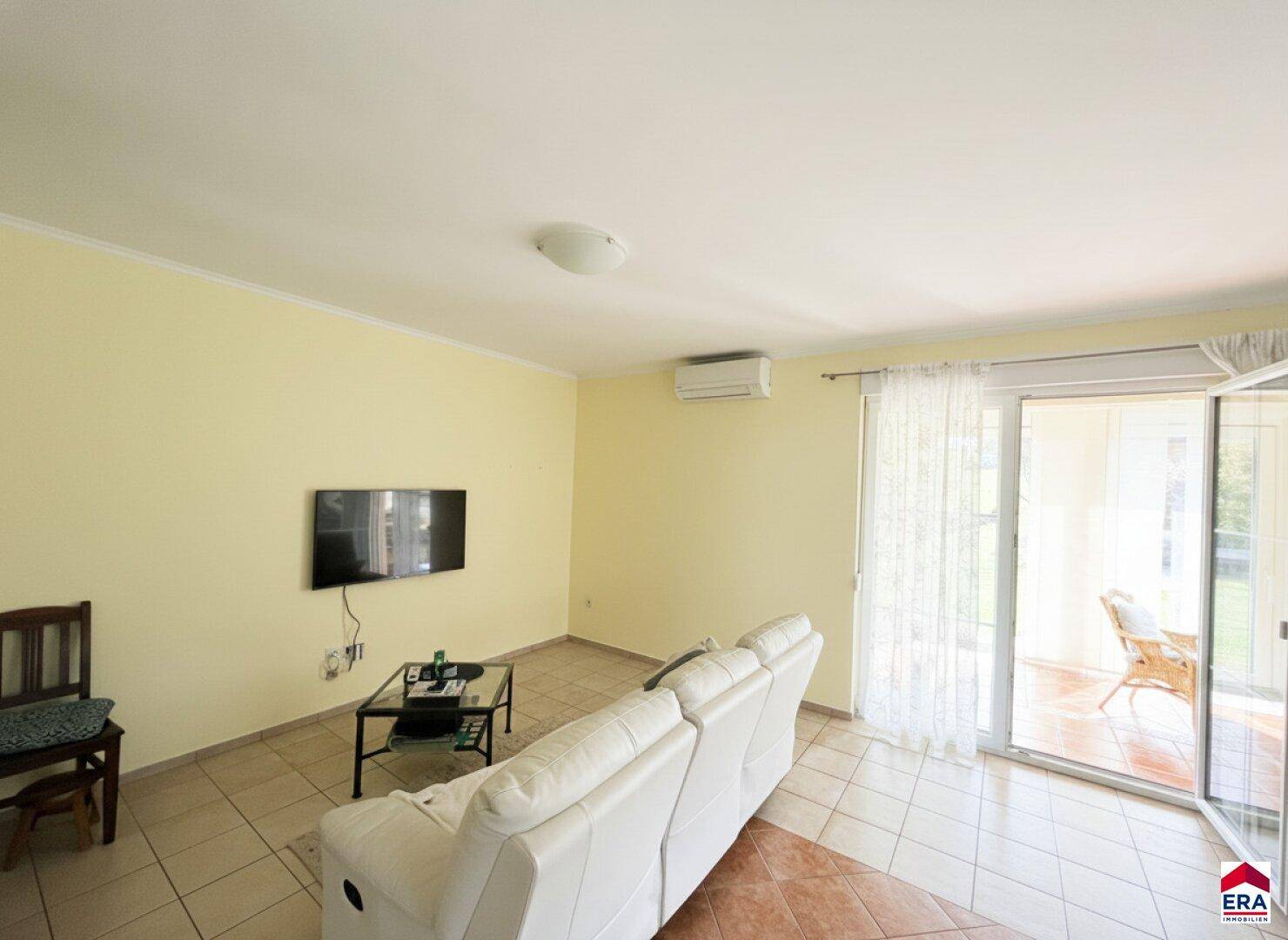 Geräumiges Wohnzimmer mit hellen Fliesen, bequemer Couch und Zugang zur Terrasse.