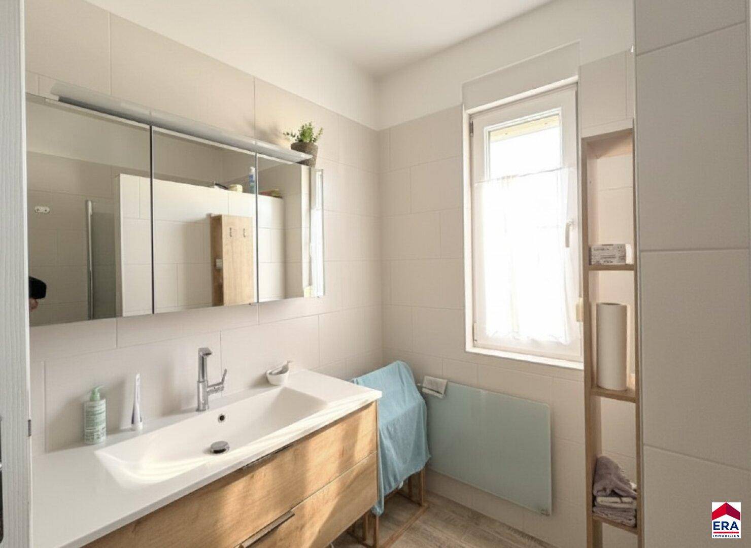 Modernes Badezimmer mit hellem Fliesenboden, Einzelwaschbecken und Fenster.