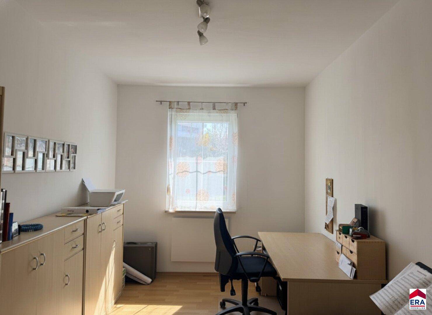 Funktionales Arbeitszimmer mit Holzmöbeln, Parkettboden und ausreichend Tageslicht.