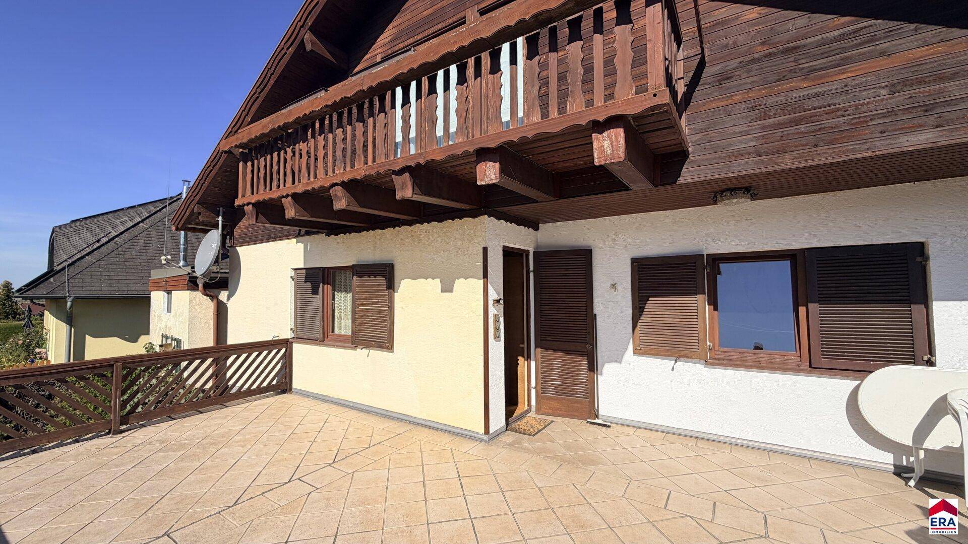 Geräumige, geflieste Terrasse im Obergeschoss mit Holzbalkon und Zugang zum Haus.
