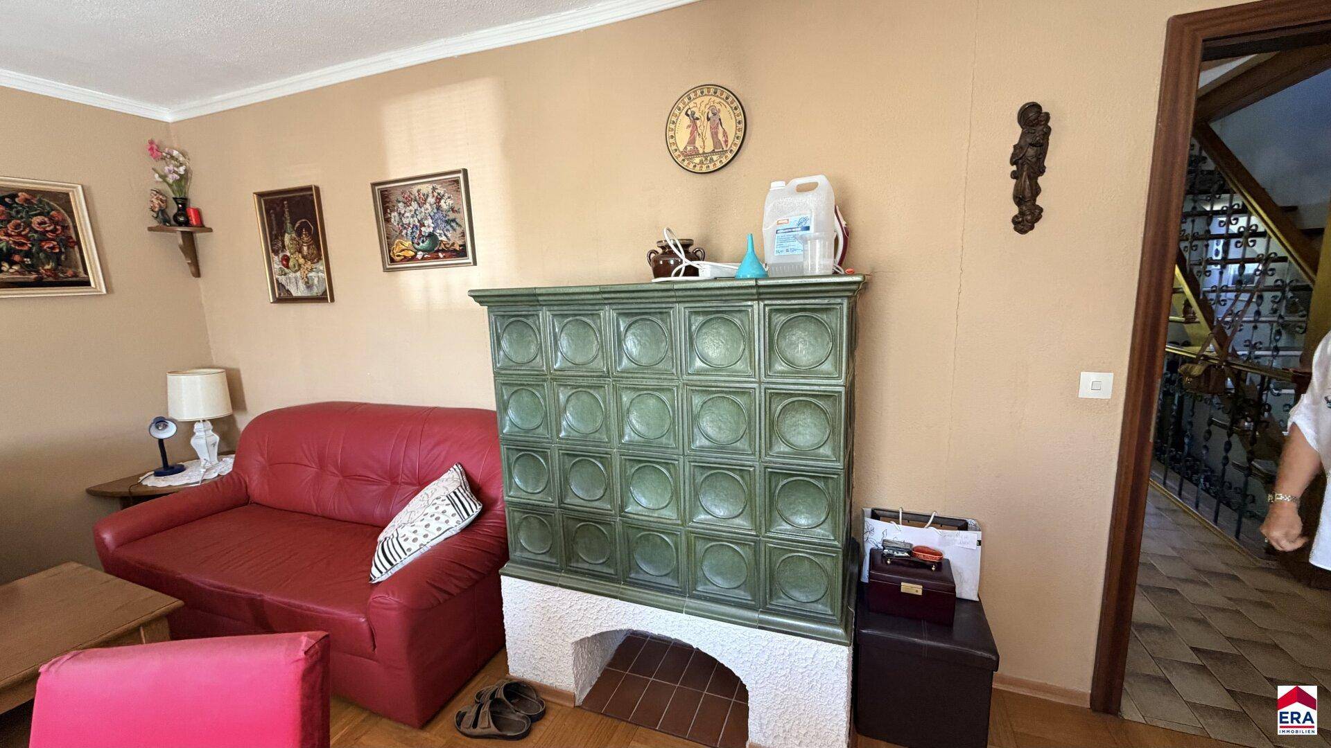 Wohnzimmer mit einem markanten grünen Kachelofen und rotem Sofa.